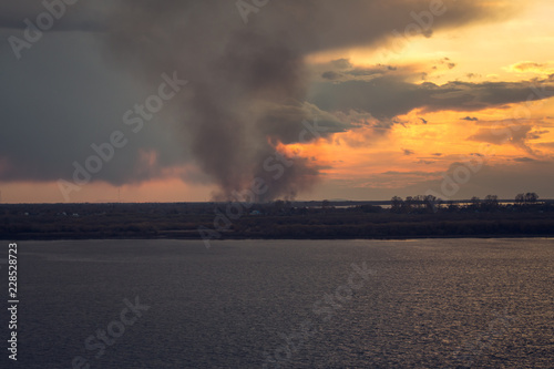 environmental problem of fire on dry grass with smoke onthe horizon inflated by a strong wind during the sunset
