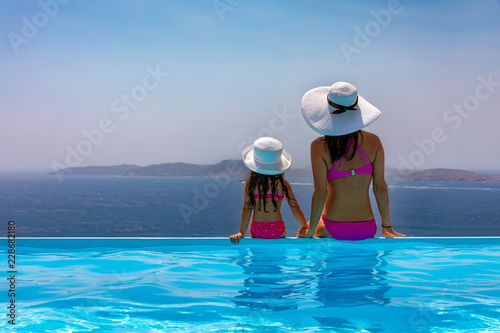 Mutter und Tochter sitzen gemeinsam im Urlaub am Pool und genießen die Aussicht auf das Meer