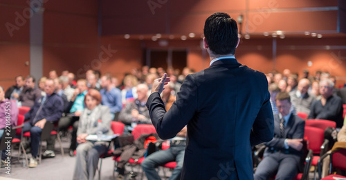 Speaker giving a talk on corporate business conference. Unrecognizable people in audience at conference hall. Business and Entrepreneurship event.