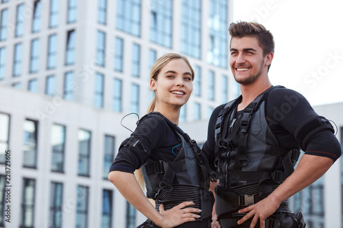 two positive young people wearing ems fitness vest and posing to the camera on the street.copy space