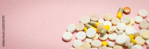 Pills of different sizes and colors on a light pink background.