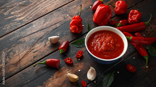 spicy hot sweet chili sauce with mix of chilli pepper, garlic and tomatoes on rustic wooden background