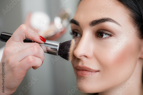 Close up of makeup artist applying light layer of matting powder while using professional brush for lady