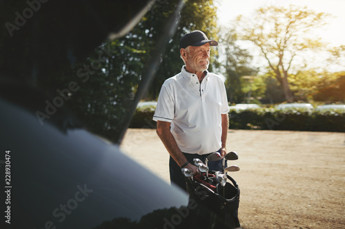 Senior man putting his golf clubs in a car trunk