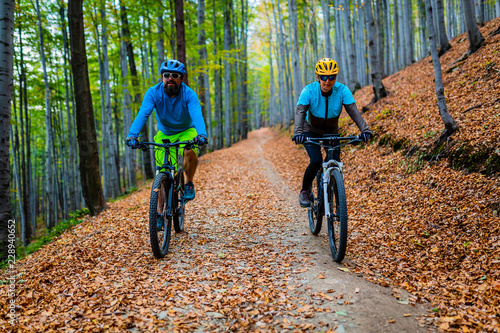 Kolarstwo, para rowerzystów górskich na szlaku rowerowym w lesie jesienią. Kolarstwo górskie w jesień krajobraz lasu. Mężczyzna i kobieta na rowerze MTB płyną pod górę szlaku.