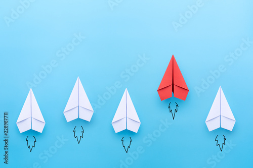 Red paper plane leading among a white planes on blue background. Business competition and Leadership concept