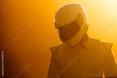 A Helmet Wearing Race Car Driver In The Early Morning Sun Looking At His Car Before Starting