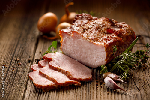 Smoked meats, sliced smoked pork loin on a wooden table with addition of fresh herbs and aromatic spices. Traditional smoked meat smoked in apple and beech wood, Natural product from organic farm