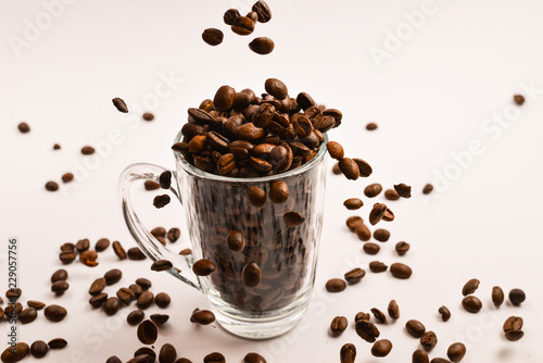 Grains of coffee are poured into a glass cup on a white background