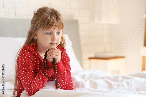 Little girl with beads praying in bedroom