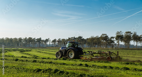 Een boer is met zijn trekker het gemaaide gras aan schudden