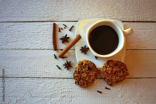 Czarna kawa w filiżance, obok anyż i laski cynamonu oraz ciastka z ziarnami