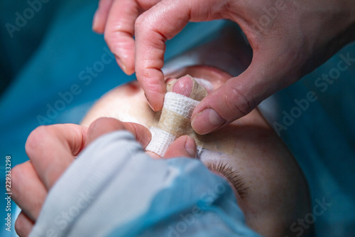 Surgeon and his assistant performing cosmetic surgery on nose in hospital operating room. Nose reshaping, augmentation. Rhinoplasty.