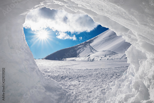 Blick aus der Schneehöhle auf verschneite Winterlandschaft mit Sonne