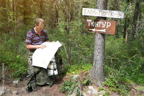 Tourist with a map near the signs. Inscriptions Tungur village, Kara Turek mountain. A man traveler got lost in a hike and is looking for a way on the map.