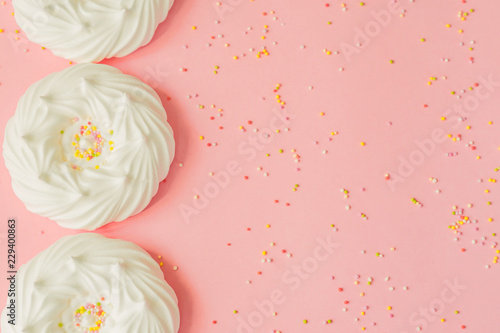 top view of homemade white air meringues and confectionery decorations on pink background