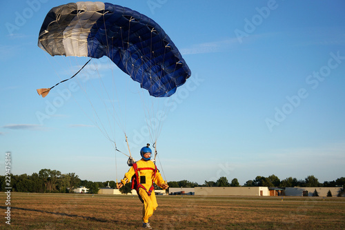 Landing of a parachuter against the background of forests and buildings. A man in a bright yellow jumpsuit is just landing