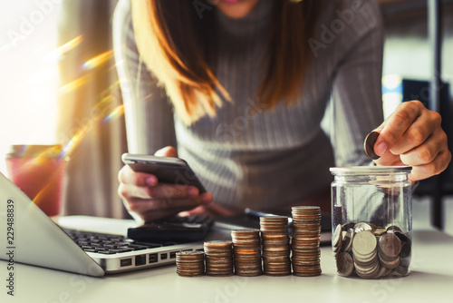 businesswoman holding coins putting in glass with using smartphone and calculator to calculate concept saving money for finance accounting