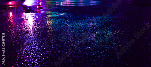 Background of wet asphalt with neon light. Blurred background, night lights of a big city, reflection, puddles. Dark neon bokeh.
