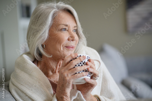  Cosy looking senior woman at home with hot drink