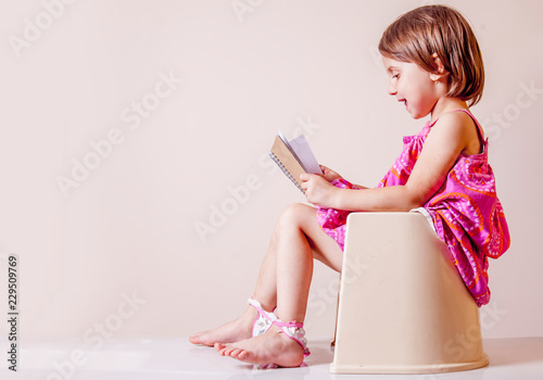Toilet busy Images. Little cute child girl with notebook sitting on toilet bowl.