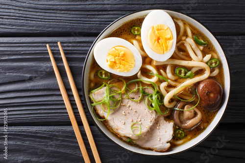 Asian style soup with udon noodles, pork, boiled eggs, mushrooms and green onions close-up on the table. horizontal top view