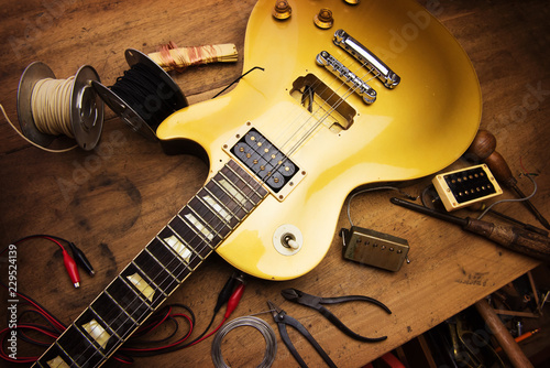 Electric guitar repair. Vintage electric guitar on a guitar repair work shop. Single cutaway solid body guitar, gold color. shallow depth of view, intentionally shot with low key shadows.