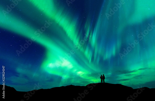 Aurora borealis with silhouette love romantic couple on the mountain.Honeymoon travel concept