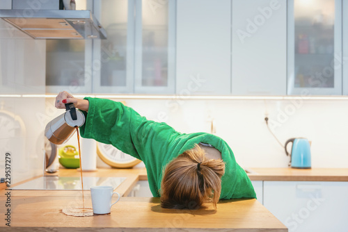 Tired woman sleeping on the table in the kitchen at breakfast. Trying to drink morning coffee