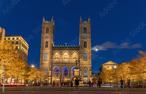 Montreal, Canada, October 20, 2018. Notre Dame Basilica from Montreal and Maisonneuve Monument illuminated at night time, during autumn season. First neo-gothic church in Canada.