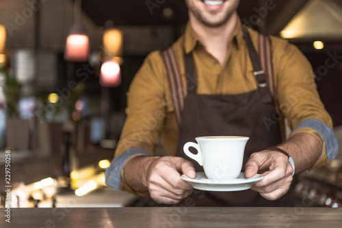 cropped shot of smiling young barista holding cup of coffee