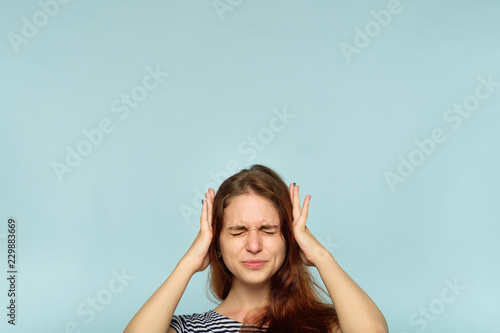 don't want to hear it. rejection refusal and denial. young woman covering ears with hands. portrait of a girl with tightly shut eyes on blue background.