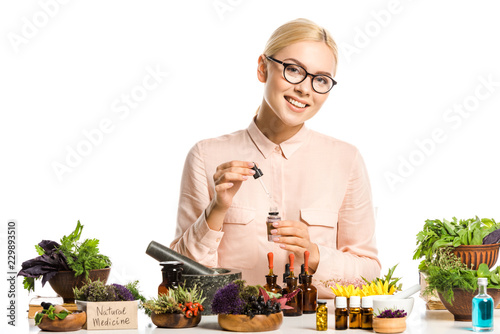 smiling woman in glasses making essential oil isolated on white and looking at camera
