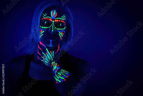 Portrait of woman with ethnic pattern, neon makeup in ultraviolet light. Body Art design of female posing in UV, painted face and hand, colourful make up