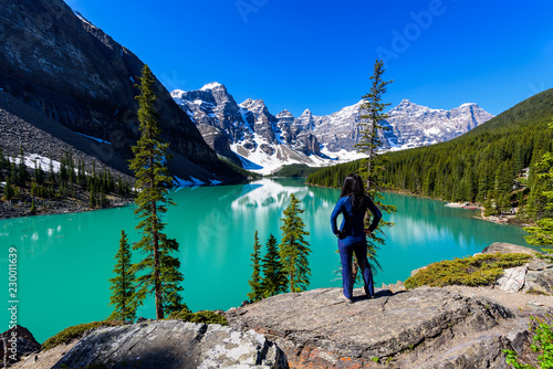 Woman on cliff admiring Moraine Lake and mountains scenic view, Rocky Mountains, Banff National Park, Alberta, Canada