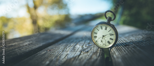 Retro Taschenuhr auf Holzbank, Himmel und bunte Blätter im Herbstlicht, Symbol für Zeit, Breitbild