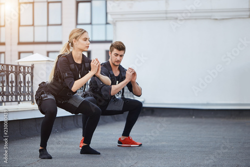 two fit young people bending knees to full squat position. side view full length photo. copy space.