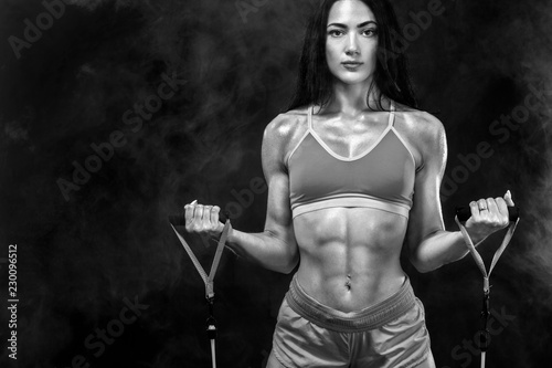 Black and white photo. Fit sports woman athlete. Workout with bands or expander in gym on black background. Copy space for fitness nutrition ads.