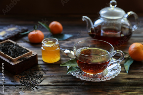 Cup of black tea, tea leaves, teapot, honey and tangerines.