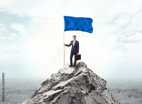 Handsome businessman on the top of the mountain with blue flag 