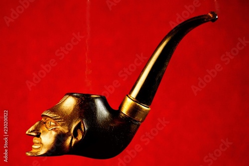 Smoking pipe-a device for ritual tobacco Smoking. Pipe Smoking tobacco cherry with vintage carved ornament profile Mephistopheles on a bright red background.