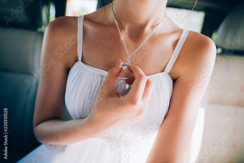 Girl in a white dress with a silver chain around her neck The bride fixes a decoration of a jewel on the neck Stylish fashionable diamond suspension girl's neck pendant pendant for women's neck