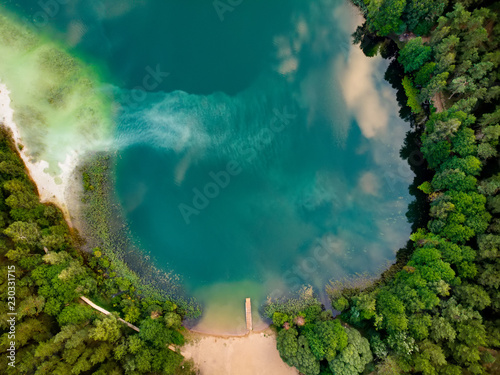 Aerial top down view of beautiful green waters of lake Gela. Birds eye view of scenic emerald lake surrounded by pine forests.