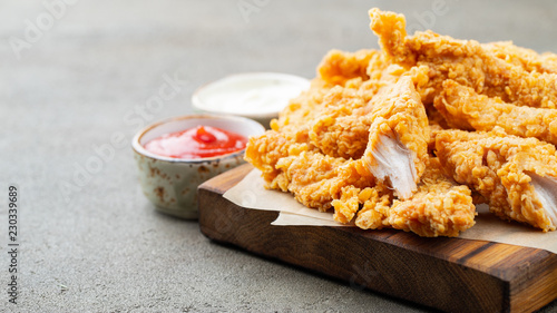 Breaded chicken strips with two kinds of sauces and fried potatoes on a wooden Board. Fast food on dark brown background. with copy space