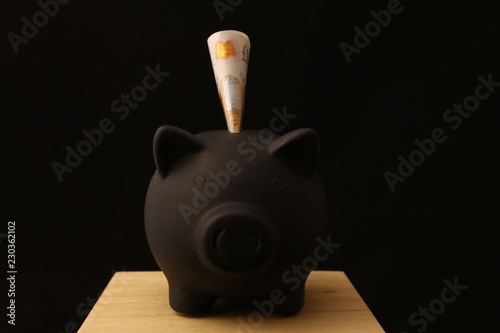 Saving money - black piggy banks with 10 pounds on black background with lightings