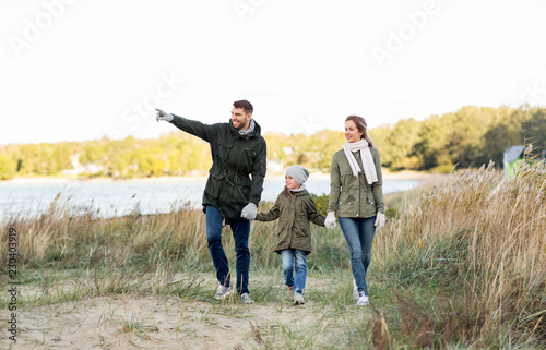 family, leisure and people concept - happy mother, father and little daughter walking along autumn beach