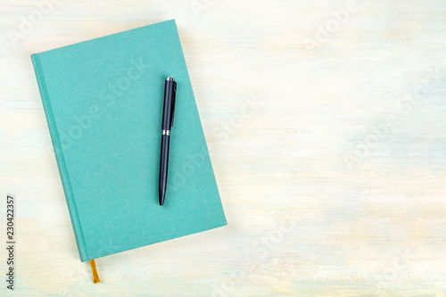 A photo of a teal blue journal with a pen, an elegant diary, notebook or planner, shot from above with copy space