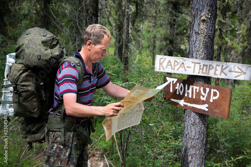 Tourist with a map near the signs. Inscriptions Tungur village, Kara Turek mountain. A man traveler got lost in a hike and is looking for a way on the map.