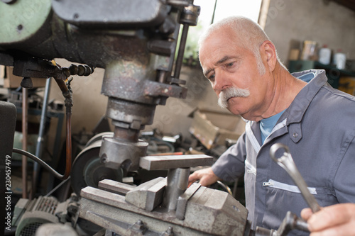 elderly worker watches processing of detail on milling machine