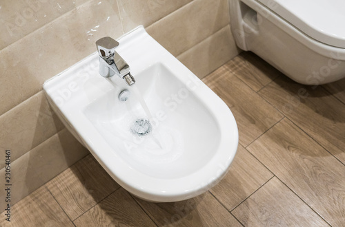 Details of white ceramic bidet with a running water in modern bathroom.